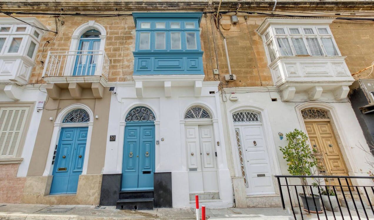 Een rij traditionele gebouwen in mediterrane stijl, met blauwe en witte deuren, balkons en een heldere lucht.