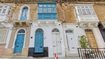 Een rij traditionele gebouwen in mediterrane stijl, met blauwe en witte deuren, balkons en een heldere lucht.