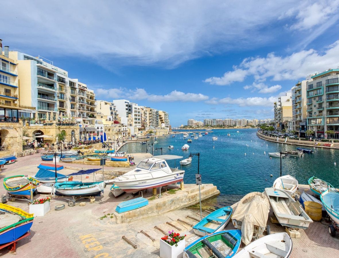 A marina with boats docked, surrounded by multi-story buildings with balconies.