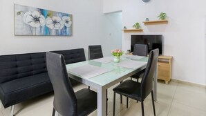 Ein modernes Wohnzimmer mit einem Esstisch mit Glasplatte, schwarzen Sofas und einem Blumenbild an der Wand.