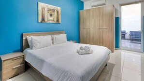 A hotel room with a bed, a nightstand, a wardrobe, and a painting on the wall. - Modern 3BR Apt with private terrace & BBQ in Gzira (Il-Gżira)