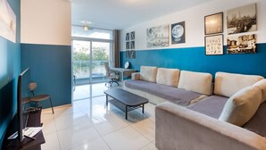 A modern living room with a sofa, a coffee table, a TV, and a desk with a chair. - Modern 3BR Apt with private terrace & BBQ in Gzira (Il-Gżira)