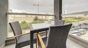 Un balcone con sedie in vimini e un tavolo, con vista su un cantiere edile e auto parcheggiate.