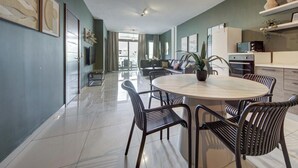 A modern living room with a round table, black chairs, a flat-screen TV, and a kitchen area with a microwave and cabinets.