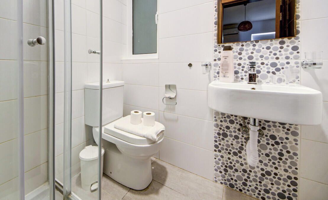 Une salle de bain avec une douche à parois de verre, des toilettes, un lavabo avec un pare-éclaboussures en mosaïque et un miroir au-dessus du lavabo.