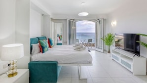A modern bedroom with a bed, a TV, a balcony with a view of the sea, and a potted plant. - Unique studio with Breathtaking views in St Pauls (San Pawl il-Baħar)