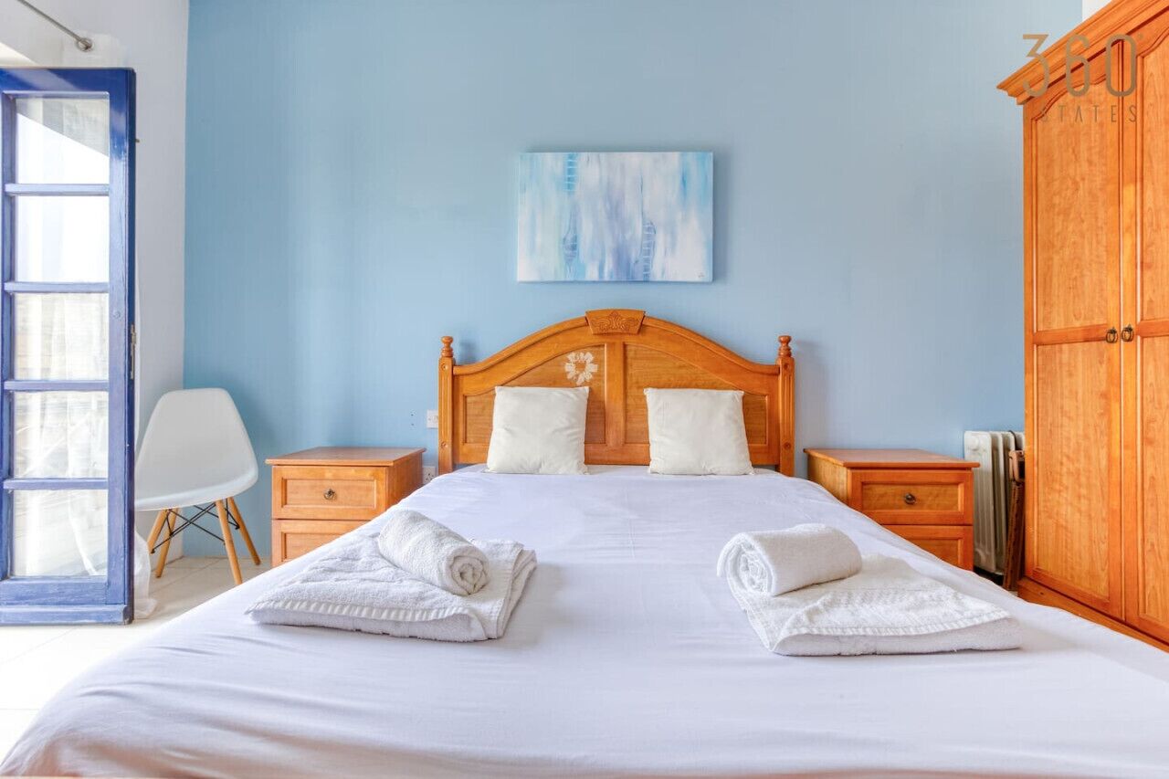 A bedroom with a wooden headboard, white bedding, two bedside tables, and a blue wall.