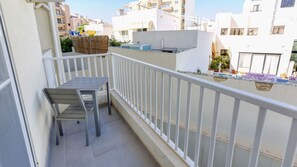 Ein Balkon mit Tisch und Stühlen, einem weißen Geländer und Blick auf benachbarte Gebäude.