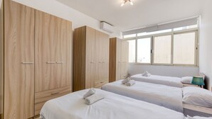 Une chambre d’hôtel avec deux lits, une grande armoire et une fenêtre avec des stores.