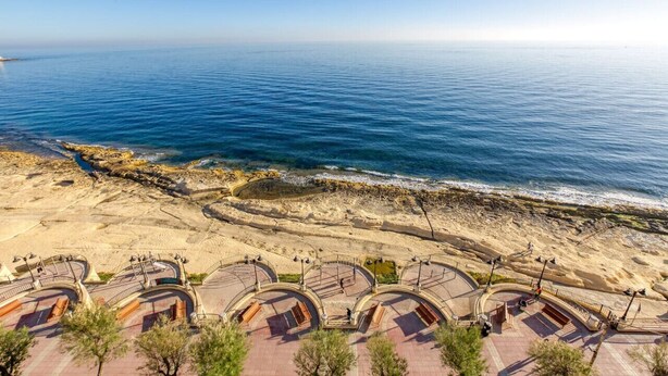 Une vue sur la côte, avec une plage et une promenade bordée de bancs.
