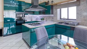 Une cuisine moderne avec des meubles de couleur turquoise, un îlot central et un coin repas comprenant une table et des chaises en verre.