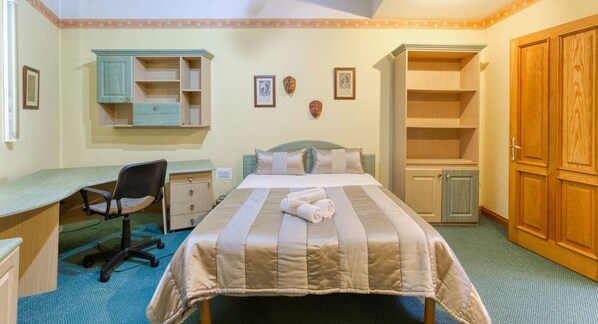 Un dormitorio con cama, escritorio, silla, armario y estanterías.