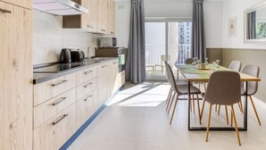 A modern kitchen with wooden cabinets, a dining table with chairs, and a large window with curtains. - Stylish 2BR home with Balcony in central Pieta (Tal-Pietà)