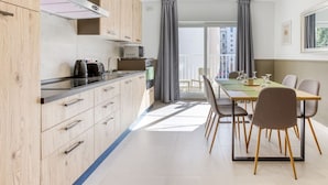 A modern kitchen with wooden cabinets, a dining table with chairs, and a large window with curtains. - Bright & Stylish 2BR home in Pieta w/WIFI & AC (Tal-Pietà)