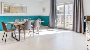 Un espace de salle à manger moderne, avec une table dressée pour quatre personnes, une grande fenêtre avec des rideaux et une vue sur l’extérieur.