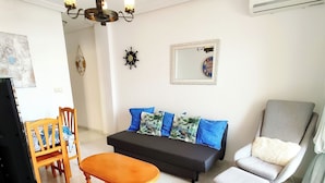 Una sala de estar con un sofá, una mesa de madera, una silla y un televisor.