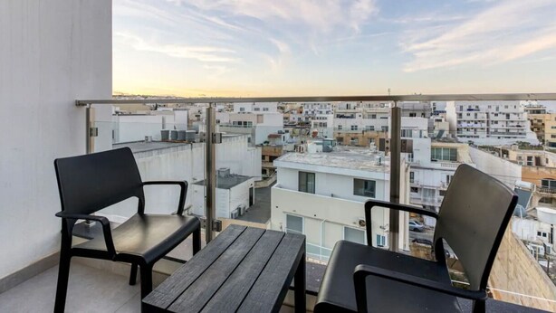 A balcony with two chairs and a table, overlooking a densely packed urban area with various buildings.