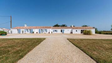 Un bâtiment blanc avec un toit recouvert de tuiles, une allée en gravier et un ciel dégagé.