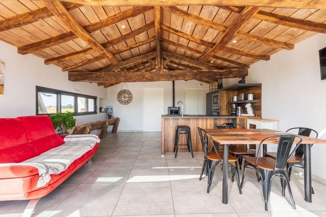 Un vaste espace de vie doté d’un plafond en bois, d’un canapé rouge, d’une table à manger avec des chaises et d’un coin cuisine avec un bar.