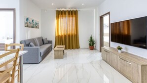 A modern living room with a grey sofa, a wooden coffee table, a flat-screen TV, and a dining area with a wooden table and chairs.