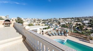 A rooftop terrace with a pool, lounge chairs, and a view of a densely built town.
