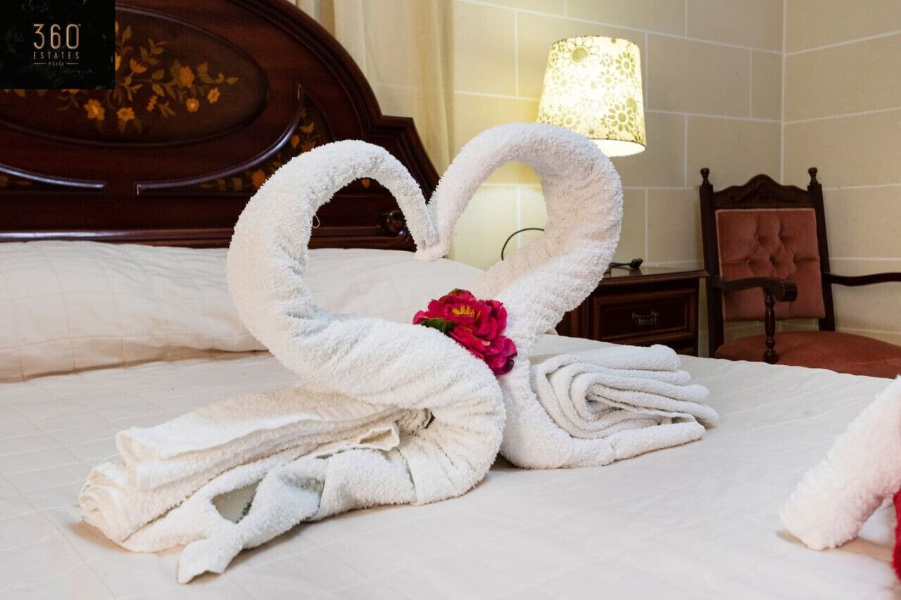Un lit avec des serviettes disposées en forme de cœur, une lampe et une tête de lit en bois.