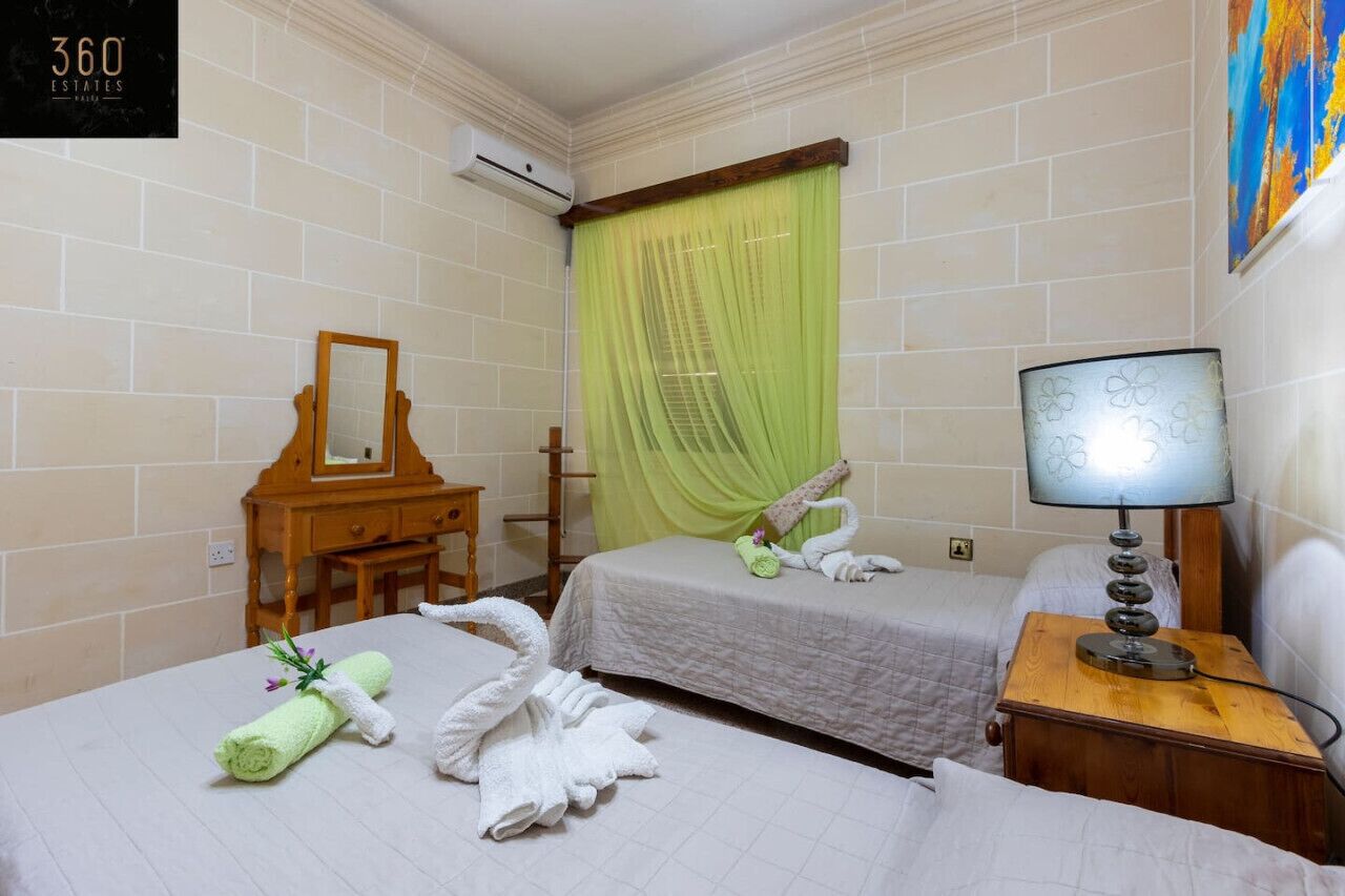Ein Hotelzimmer mit zwei Betten, einem Holzschrank, einem Schreibtisch, einer Lampe und einem grünen Vorhang.
