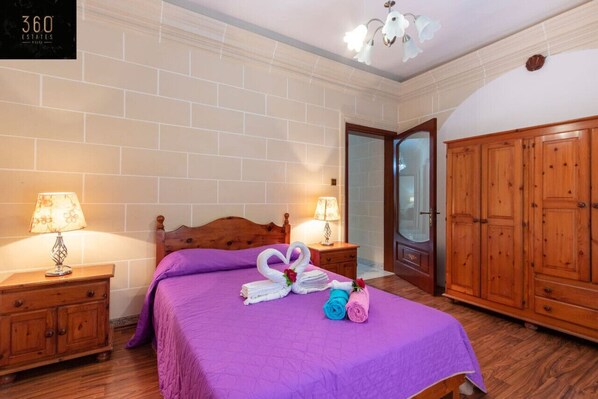 A hotel room with a wooden bed, purple bedding, two bedside tables with lamps, a wardrobe, and a sign on the wall.