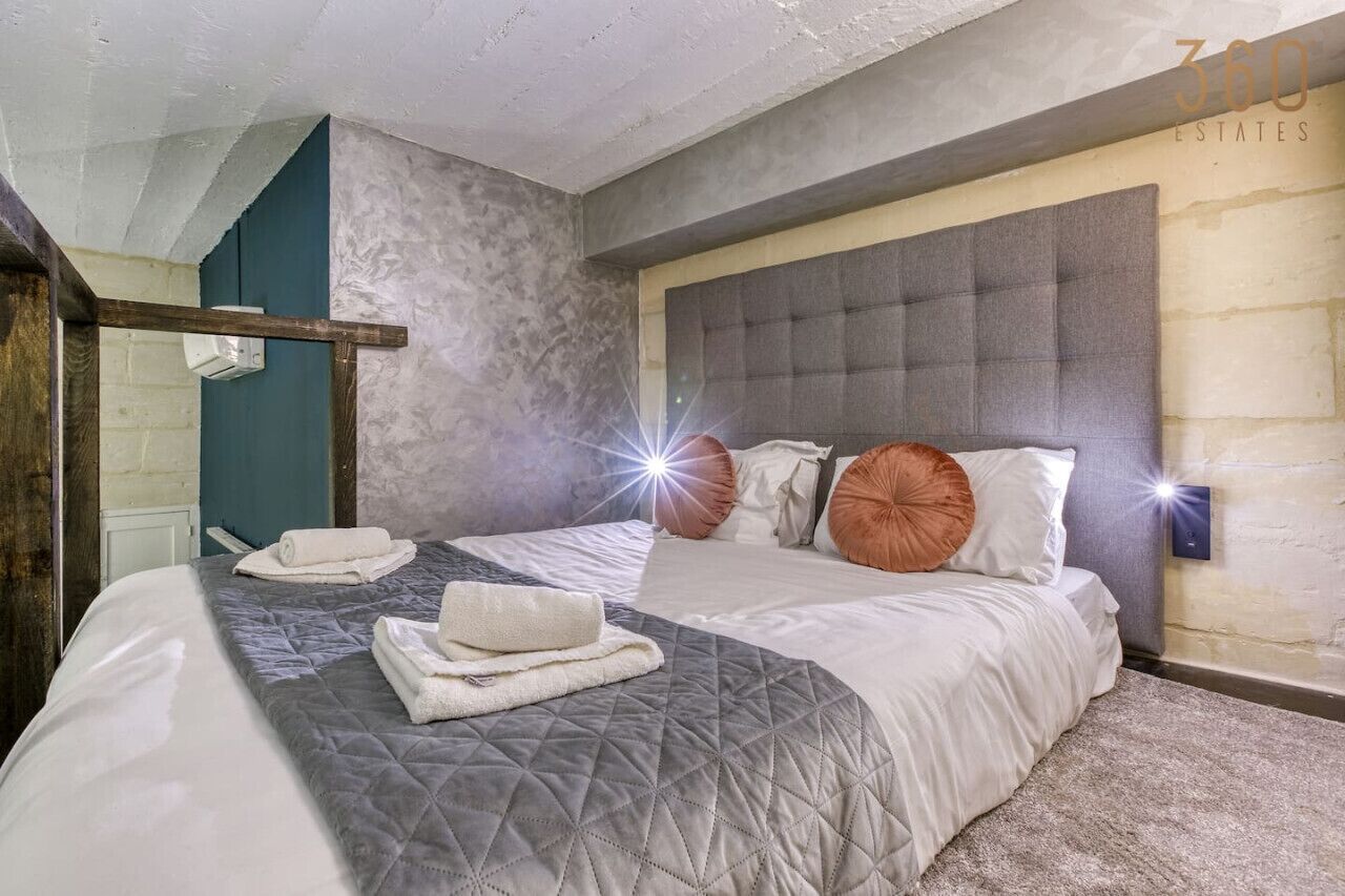 Une chambre moderne avec un grand lit, une tête de lit grise et un luminaire fixé au mur.