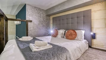 Une chambre moderne avec un grand lit, une tête de lit grise et un luminaire fixé au mur.