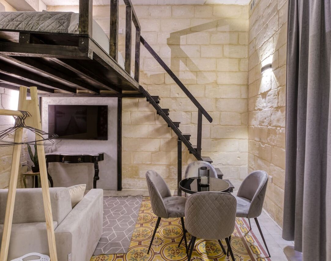 Une pièce avec un lit en mezzanine, un escalier, une télévision, une table avec des chaises et un sol à motifs.