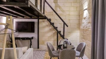 Une pièce avec un lit en mezzanine, un escalier, une télévision, une table avec des chaises et un sol à motifs.