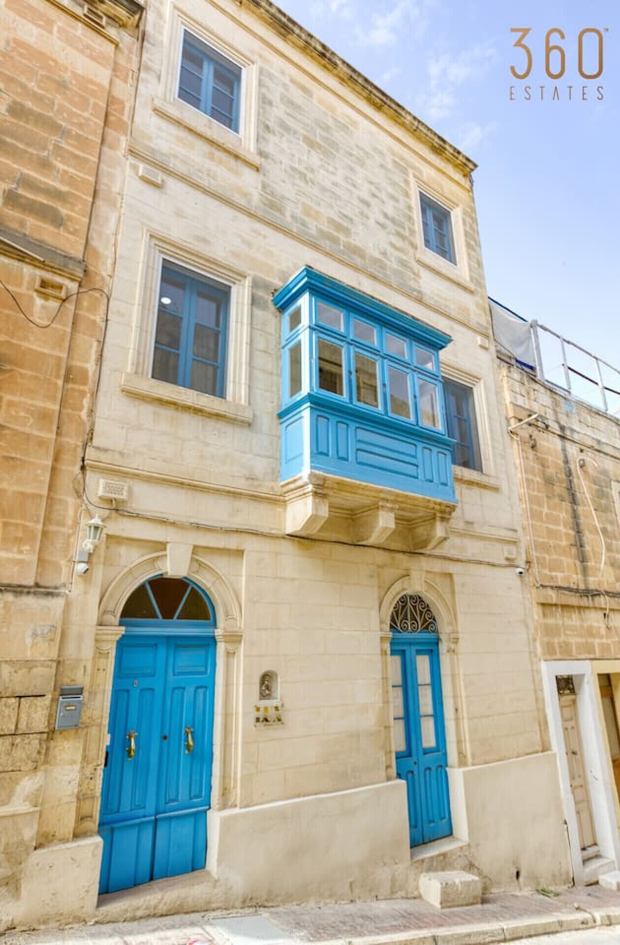 Un edificio a due piani con facciata in pietra, porte blu e un balcone con decorazioni blu.