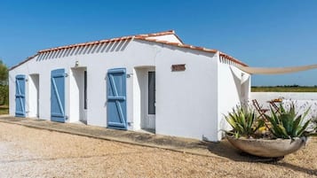 A white building with blue shutters, a gravel driveway, and a large planter with plants.