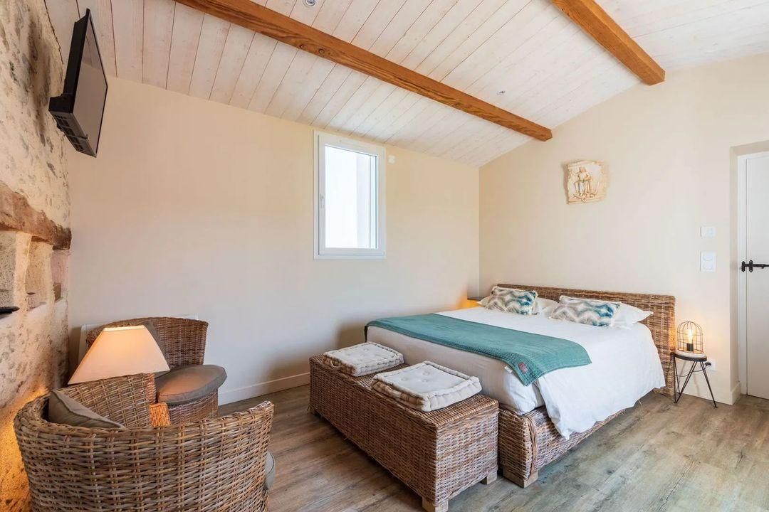 A bedroom with a bed, wicker furniture, a window, and a wooden ceiling.