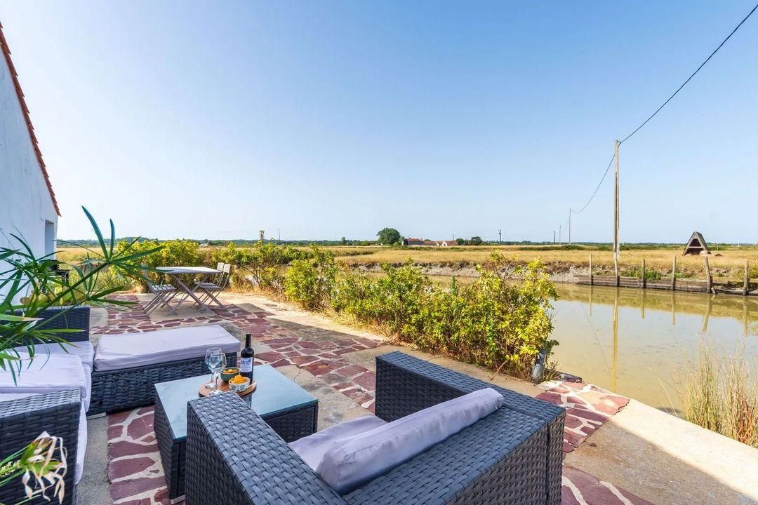Een terras buiten met rieten meubilair, een tafel en uitzicht op een waterpartij en het verre landschap.