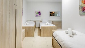 Ein Schlafzimmer mit zwei Einzelbetten, einem Holzschrank, einem kleinen Nachttisch, einem Spiegel und einem an der Wand hängenden Kunstwerk.