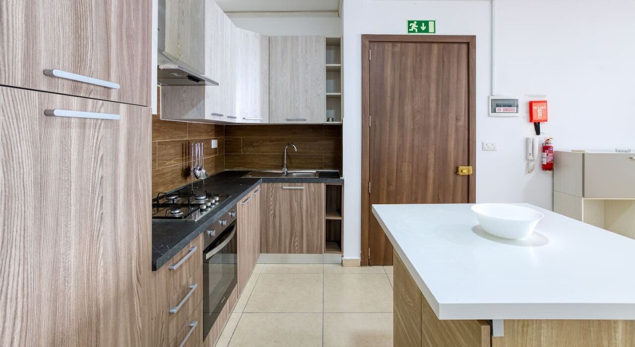 Una cucina moderna con mobili in legno, piano cottura a gas, lavello e un ripiano di lavoro bianco.