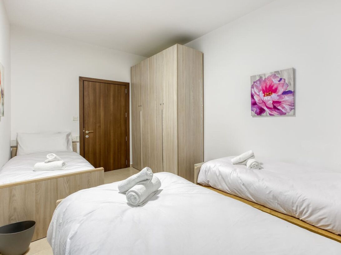 A hotel room with two beds, a wooden wardrobe, and a painting of a flower on the wall.