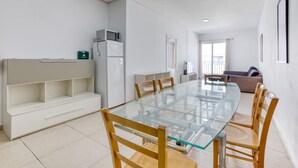 Ein moderner Essbereich mit einem Glastisch, Holzstühlen, einem weißen Sofa und einem weißen Schrank.