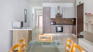 A modern kitchen with wooden cabinets, a microwave, and a stove. There is a glass dining table with chairs. - Spacious 4BR home with private balcony in Swieqi (Is-Swieqi)