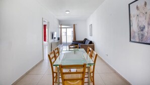 A spacious living area with a glass dining table, wooden chairs, a sofa, and a mounted artwork. - Spacious 4BR home with private balcony in Swieqi (Is-Swieqi)