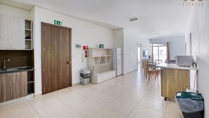 A spacious kitchen with a wooden cabinet, a sink, and a trash bin. There is a dining area with a table and chairs. - Spacious 4BR home with private balcony in Swieqi (Is-Swieqi)