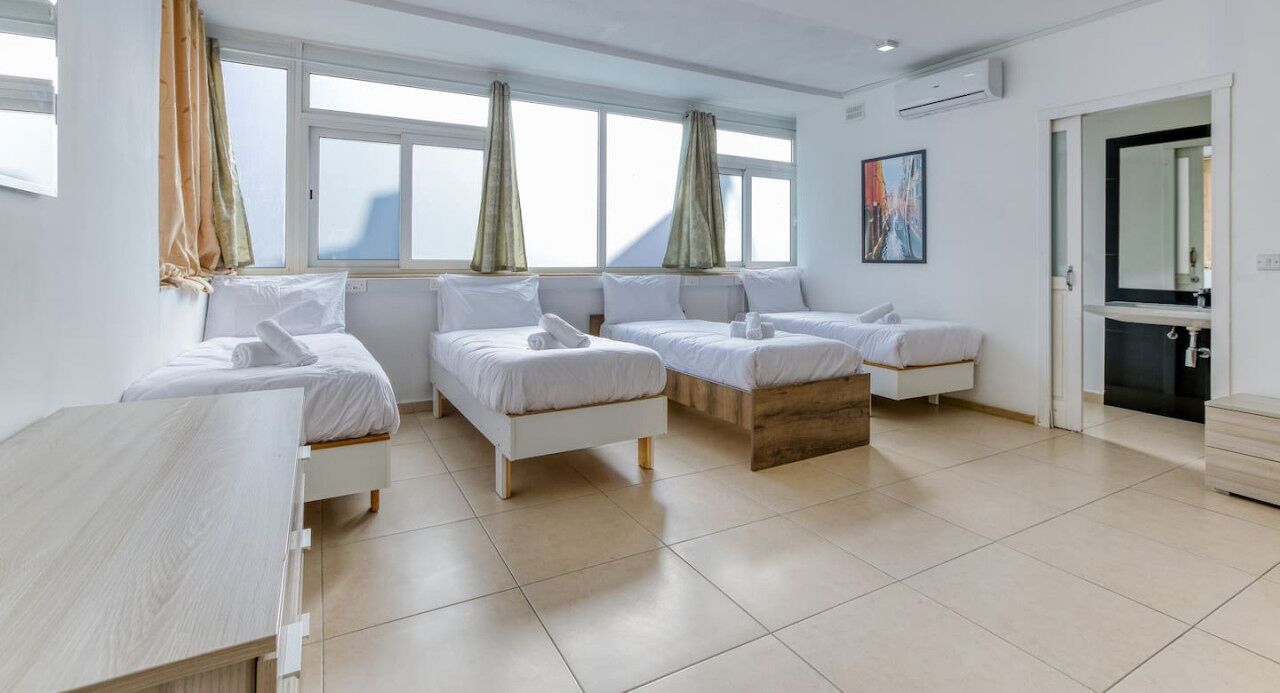 Hotelkamer met drie bedden, een groot raam met gordijnen, een schilderij en een zichtbare badkamer door een geopende deur.