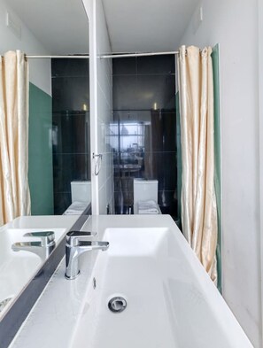 Un baño moderno con un lavamanos grande de color blanco, dos llaves y un box de ducha de vidrio.
