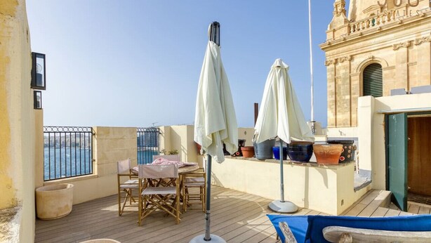 A rooftop terrace with a table and chairs, umbrellas, and potted plants.