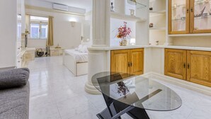 A spacious living area with a glass coffee table, a sofa, and a dining table. There are wooden cabinets and a white fireplace.