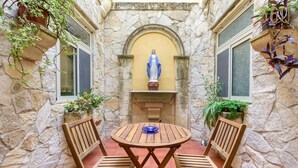 A stone-walled patio with a statue, a round wooden table, and two wooden chairs.