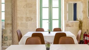 A room with a long table, six chairs, a potted plant, a fire extinguisher, and a window with green shutters. - Spectacular 5BR Townhouse located in Sliema (Tas-Sliema)