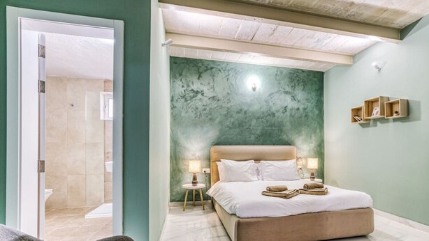 A bedroom with a large bed, two bedside tables with lamps, a green accent wall, and a door leading to another room. - Spectacular 5BR Townhouse located in Sliema (Tas-Sliema)